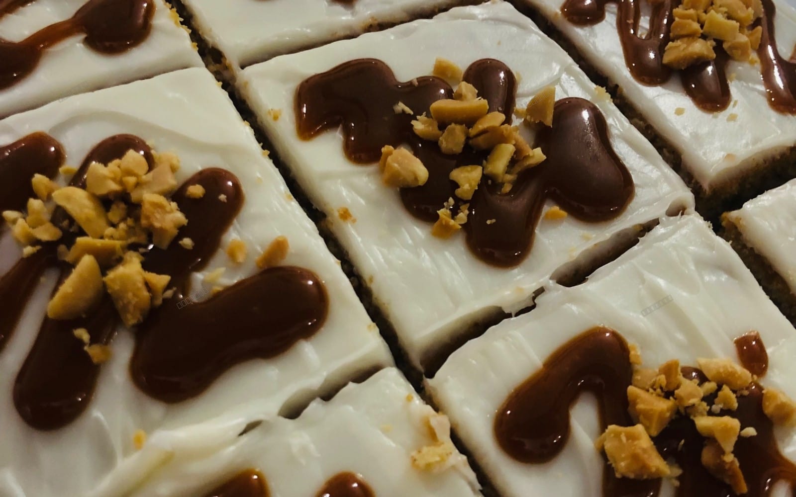 Caramel peanut carrot cream dessert bars with creamy white frosting and chocolate drizzle