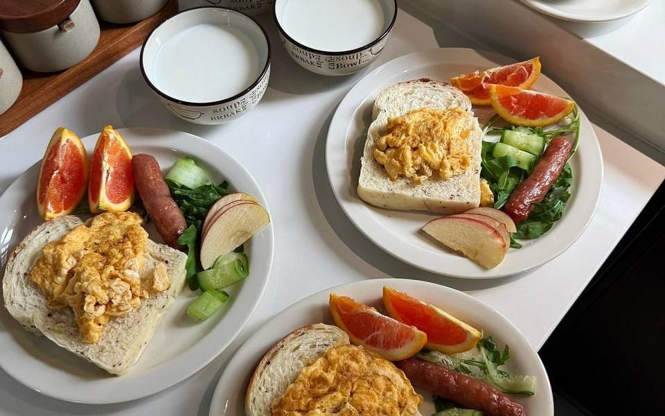 Three plated breakfast meals with bread, sausage, vegetables, and fruit, part of a mixed food lifestyle fashion