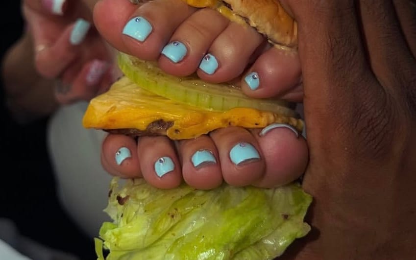 Close-up of hands holding bright green and yellow street food with blue-painted fingernails