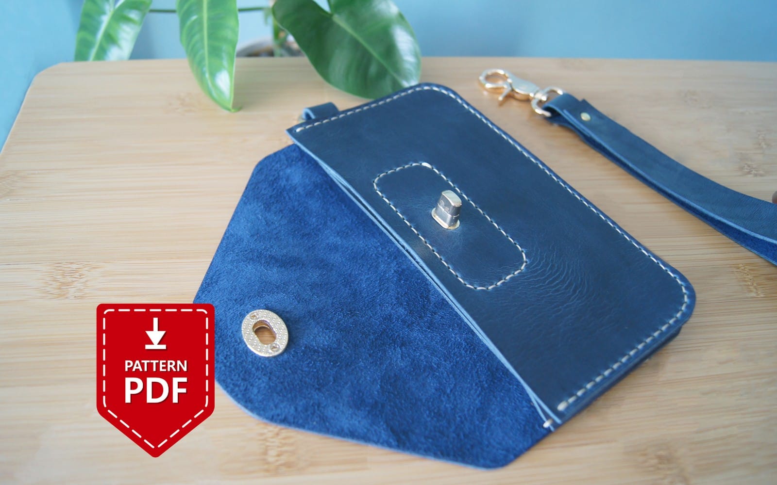 Blue leather envelope clutch on a wooden table with a downloadable free PDF pattern icon badge