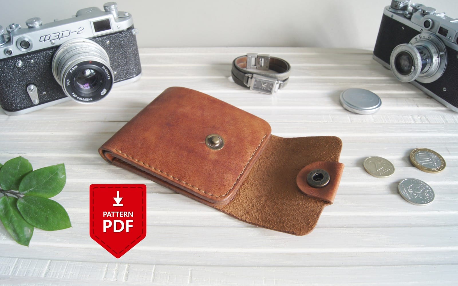 Brown leather bifold wallet pattern PDF shown on a tabletop with coins, cameras, and a download icon
