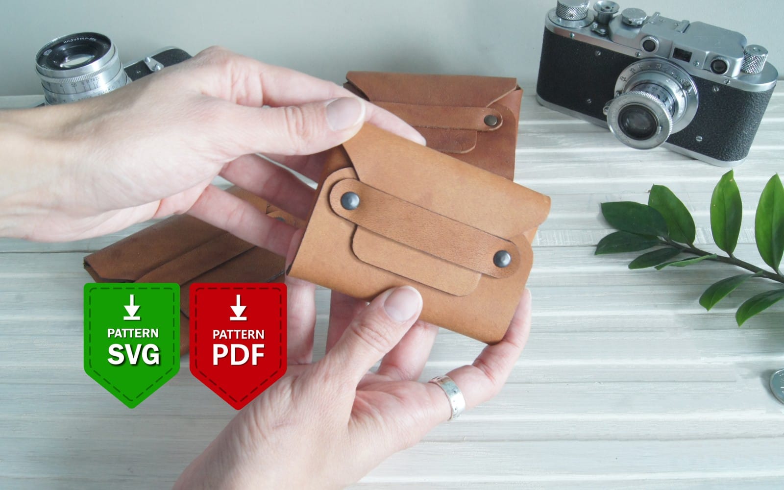 Hand holding a brown leather fold cardholder with PDF pattern download icons on a craft workspace background