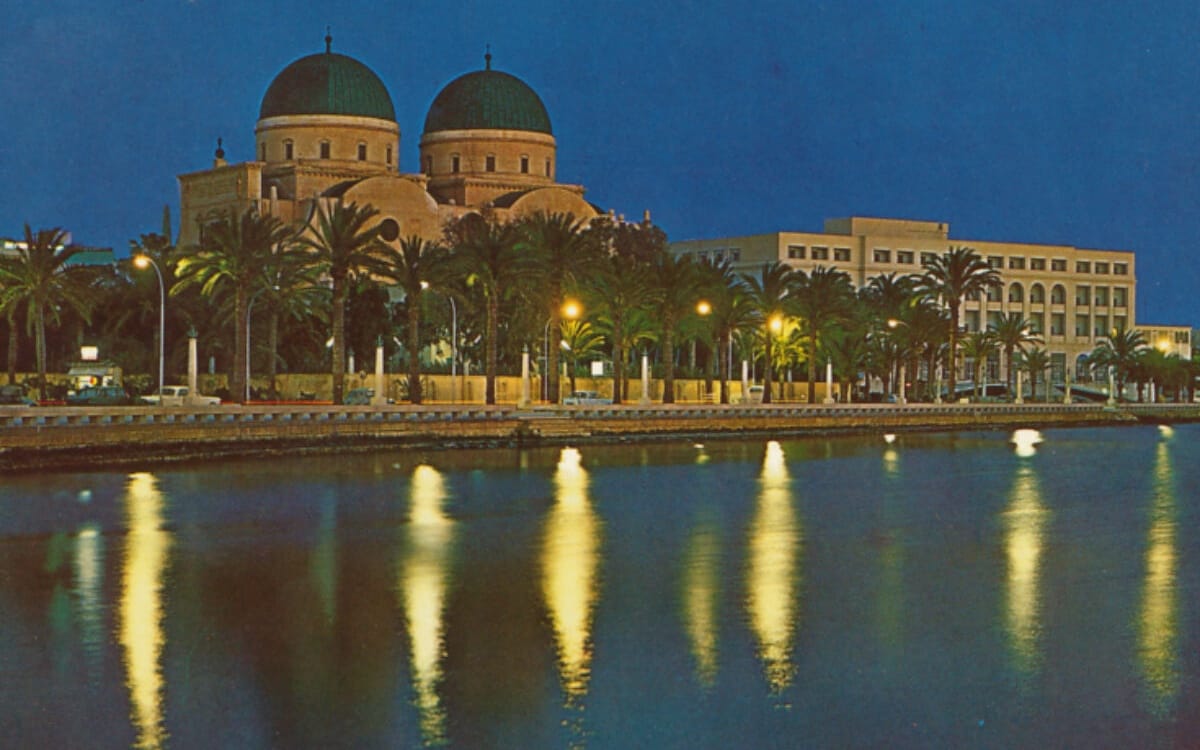Night waterfront cityscape in Benghazi with domed mosque and palm-lined buildings reflecting in calm water weekly guide
