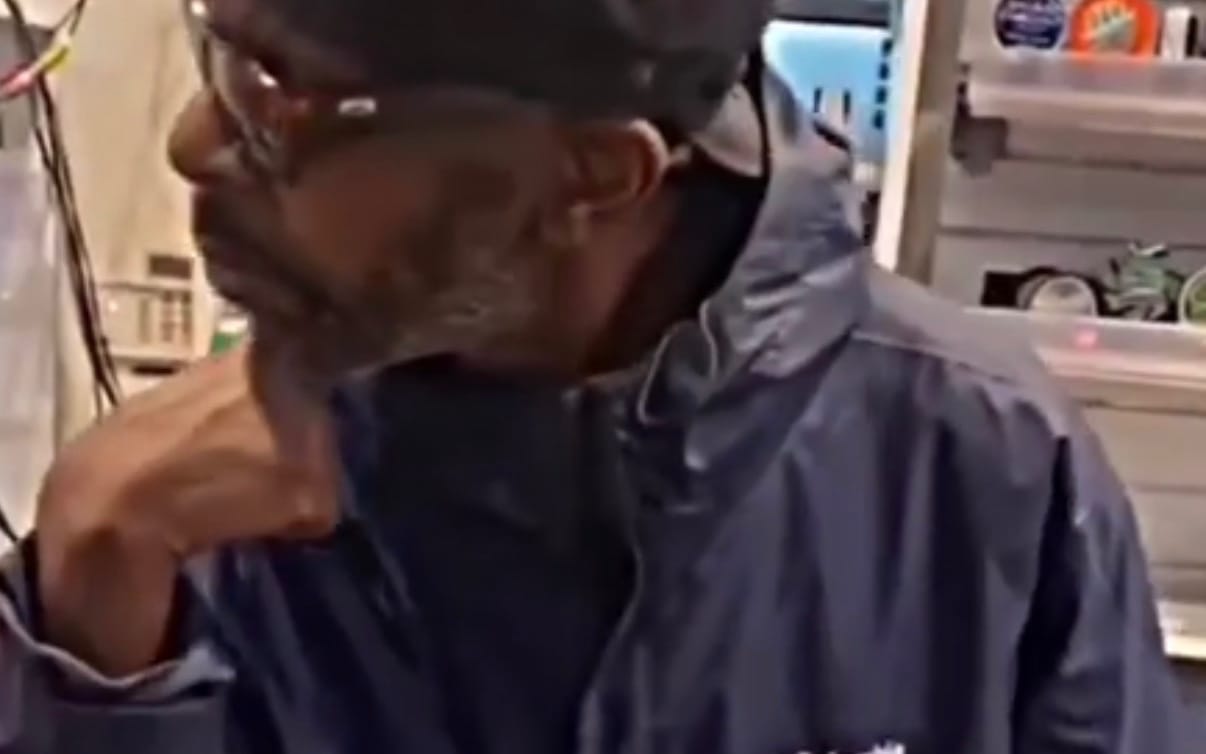 Close-up of a man in a hooded sweatshirt adjusting his face, people candid video still